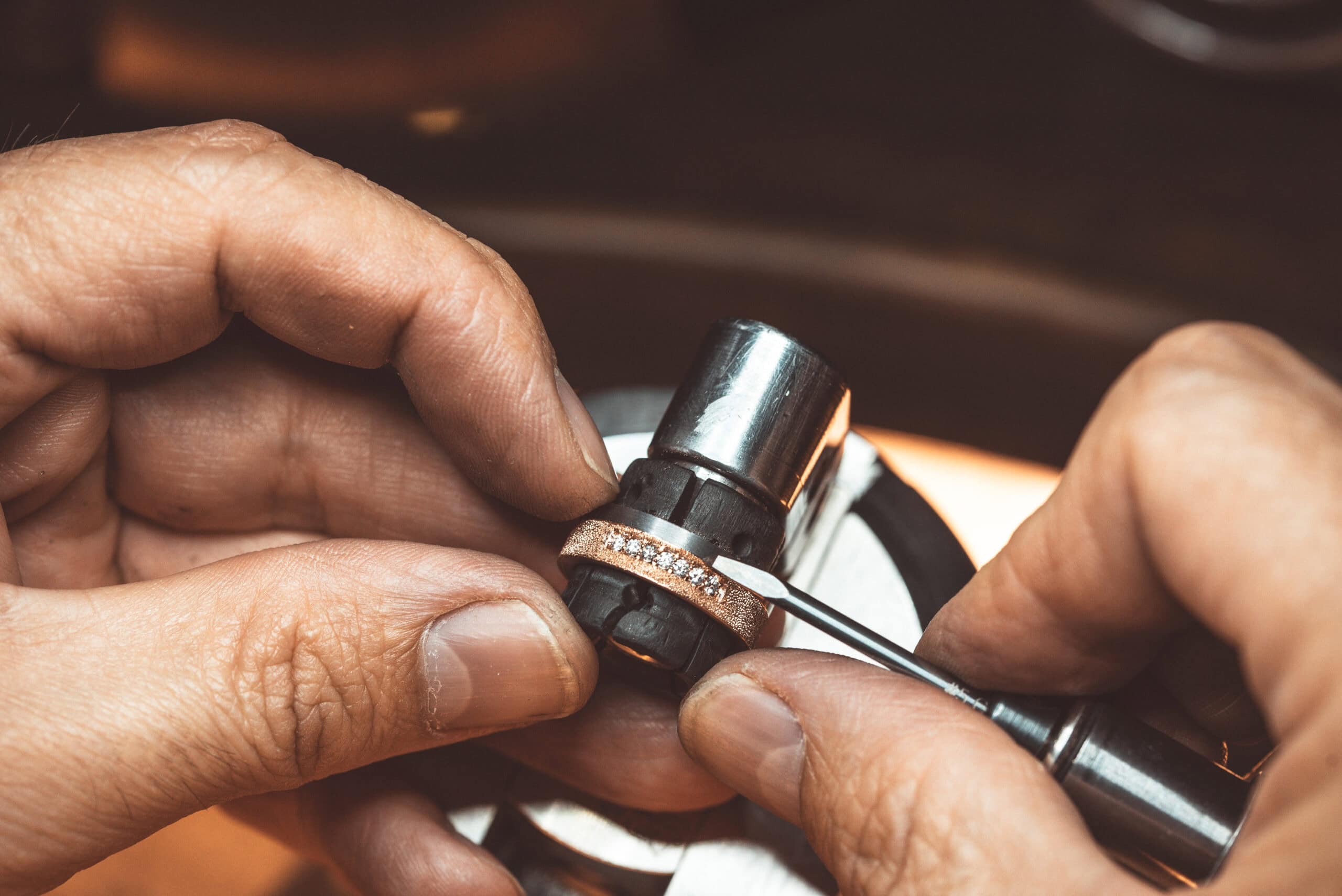 Two hands are setting diamonds in a tantalum ring